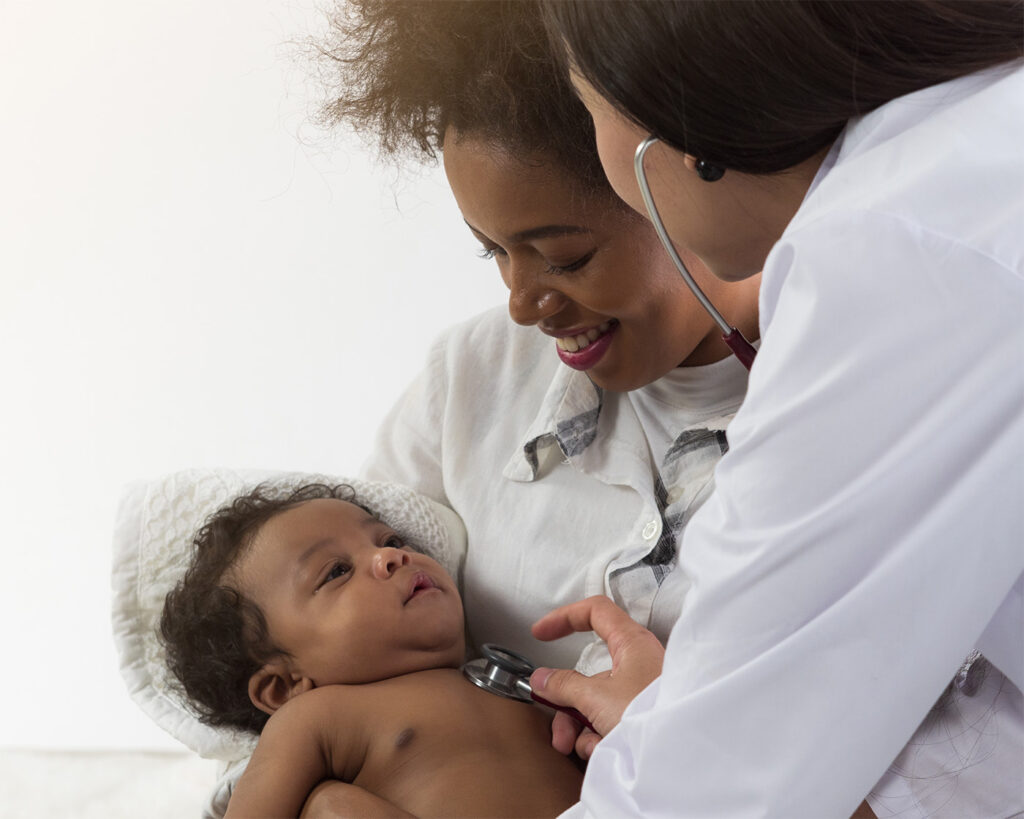 Female health care provider listening to an infants heart beat with a stethoscope. The infant is being held in the arms of their mother.