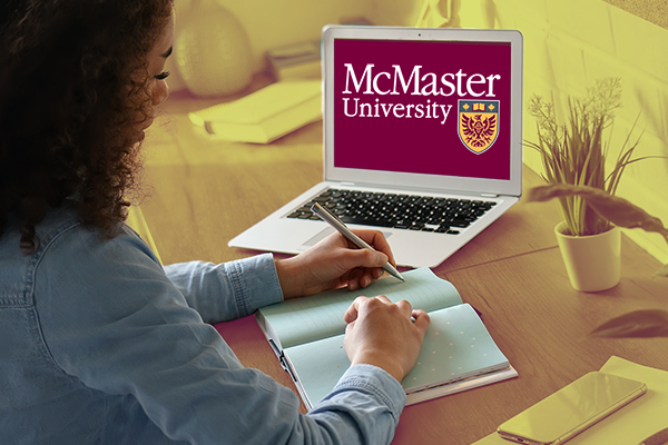 A woman writing in her notebook at her desk an in front of a laptop displaying the McMaster University logo.