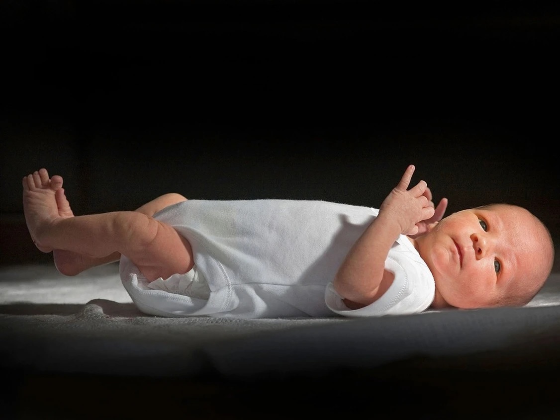 infant laying on their back wearing a white onesie