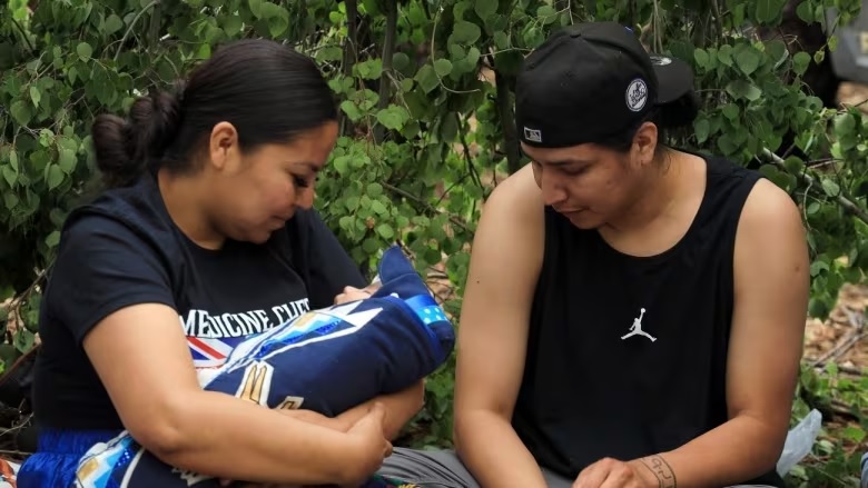An Indigenous midwife is holding an infant next to the infant's father.